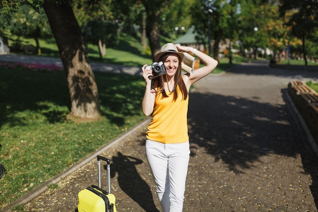 Mujer de turista bastante viajero con sombrero con maleta mapa de la ciudad tomar fotografías en la cámara de fotos retro vintage en la ciudad al aire libre. Chica viajando al extranjero para viajar durante una escapada de fin de semana. Estilo de vida de viaje turístico.