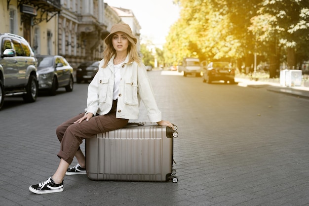 Mujer turista en la calle de una ciudad europea, turismo en Europa. Estilo de ropa urbana. sentado en una maleta grande mirando al fotógrafo