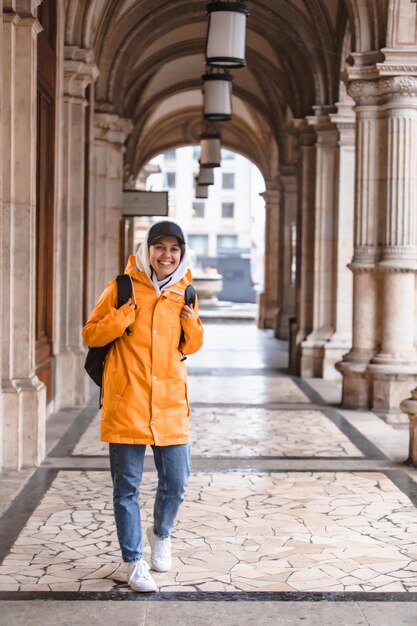 Mujer turista caminando con mochila en impermeable amarillo turismo de ciudad