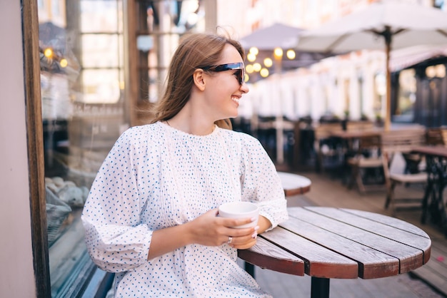 Mujer turista disfruta de la arquitectura de las calles de la ciudad con una taza de café Concepto de viaje y vacaciones