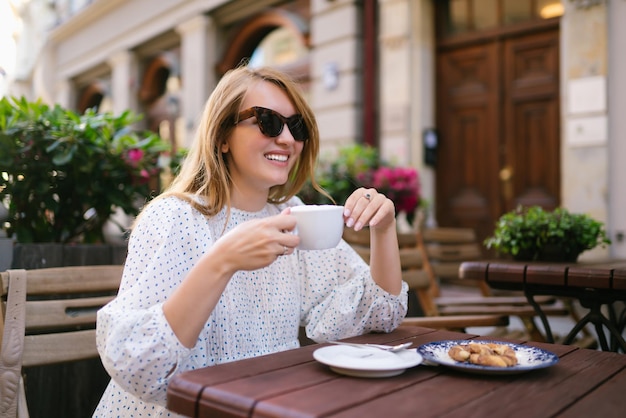 Mujer turista disfruta de la arquitectura de las calles de la ciudad con una taza de café Concepto de viajes y vacaciones