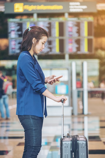 Mujer turista con equipaje en el aeropuerto. Feliz joven viajero con teléfono móvil.