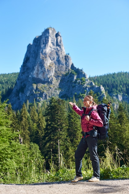 Mujer turista feliz. Un hermoso paisaje de montañas, bosques y cielo azul sobre ellos en un día soleado.