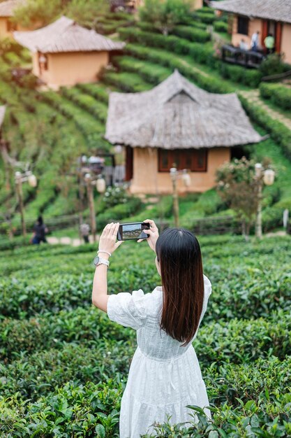 Mujer turista feliz con vestido blanco tomando fotos con un teléfono inteligente móvil en el hermoso jardín de té Viajero que visita el pueblo tailandés de Ban Rak Mae Hong Son Tailandia viajes vacaciones y concepto de vacaciones