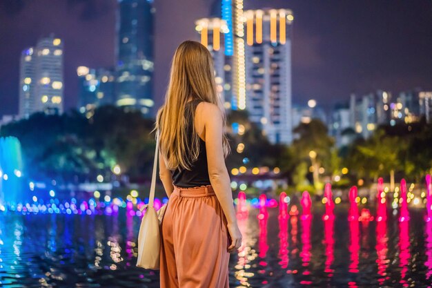 Mujer turista en el fondo de una fuente colorida en el lago por la noche cerca de las Torres Gemelas con la ciudad en el fondo Kuala Lumpur Malasia