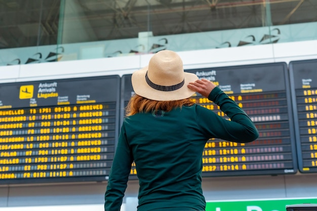 Mujer turista irreconocible en el aeropuerto mirando información en pantallas en la terminal de conexión