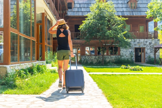 Mujer turista con una maleta de vacaciones rurales llegando a una cabaña de montaña