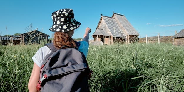 Una mujer turista se para y mira una casa de madera abandonada. Chica señala una casa vieja.