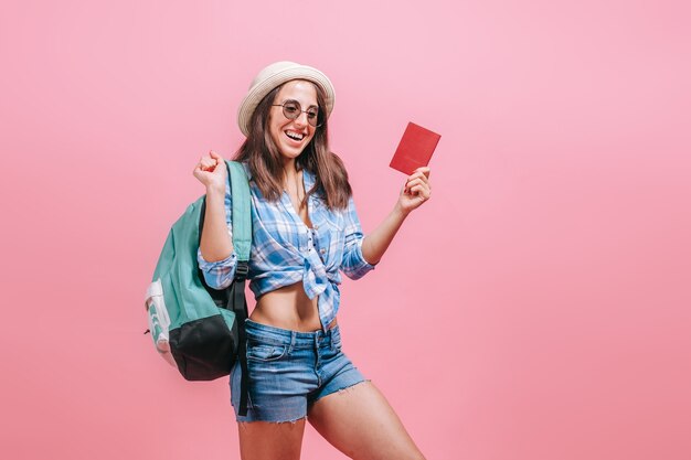 La mujer turista con mochila está mostrando el pasaporte en una pared rosa.