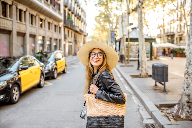 Foto mujer turista con sombrero cruzando la calle con taxi pintado de amarillo viajando en la ciudad de barcelona