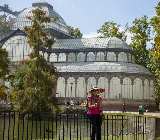 Foto mujer turista tomando selfie en el parque del retiro de madrid junto al palacio de cristal