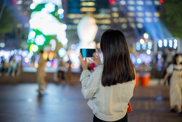 Mujer turista usa su teléfono celular para tomar fotos en la ciudad por la noche