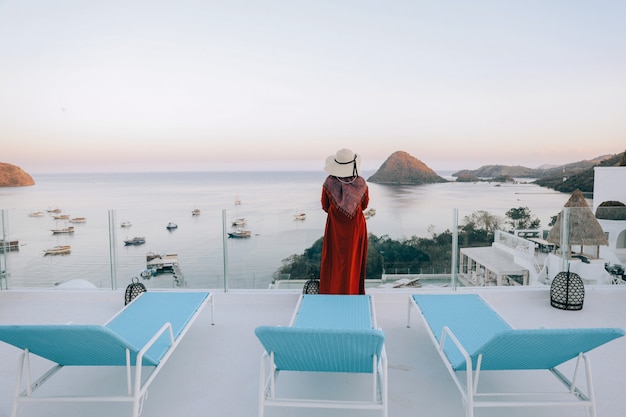 Mujer turista de vacaciones en busca de paisaje marino con puerto desde el balcón superior