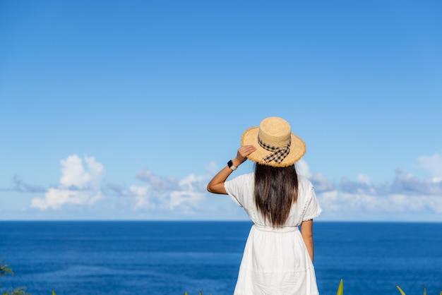 Mujer turista con vestido blanco y mira el mar en verano