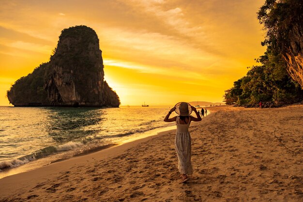 Mujer turista en vestido blanco y sombrero caminando en Phra nang Cave Beach al atardecer Railay Krabi Tailandia vacaciones viajes verano Wanderlust y concepto de vacaciones