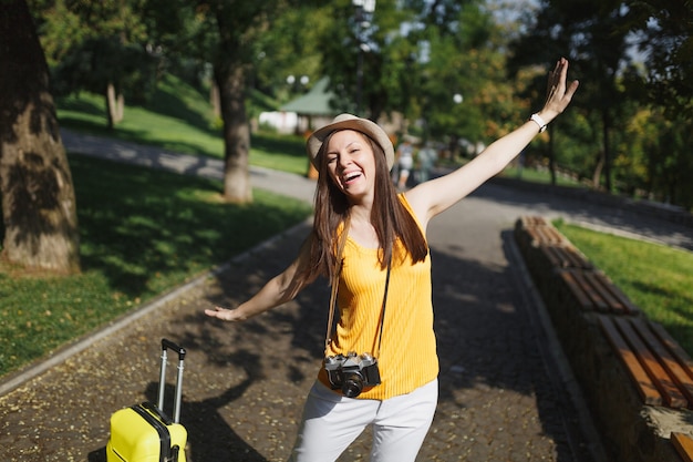 Mujer de turista viajero alegre con sombrero con maleta cámara de fotos vintage retro extendiendo las manos como alas en la ciudad al aire libre. Chica viajando al extranjero para viajar en una escapada de fin de semana. Estilo de vida de viaje turístico.