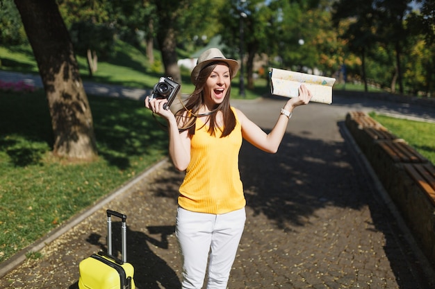 Mujer de turista viajero con mapa de la ciudad de maleta con cámara de fotos vintage retro extendió las manos gritando en la ciudad al aire libre. Chica viajando al extranjero para viajar en una escapada de fin de semana. Estilo de vida de viaje turístico.