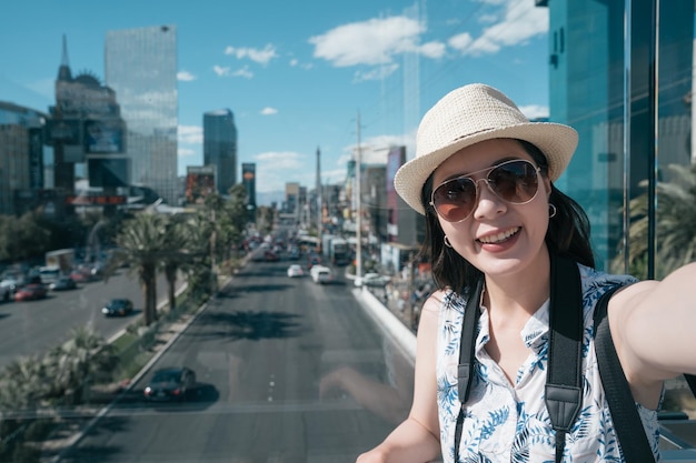 mujer turista visitando las vegas en vacaciones de verano. estudiantes de intercambio chica tomando selfie en ciudad moderna sonriendo en vacaciones de viaje de día soleado. una viajera feliz se hace un autorretrato en el paso elevado