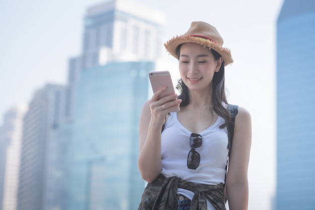 Mujer turística solitaria asiática hermosa que sonríe y que mira el teléfono móvil