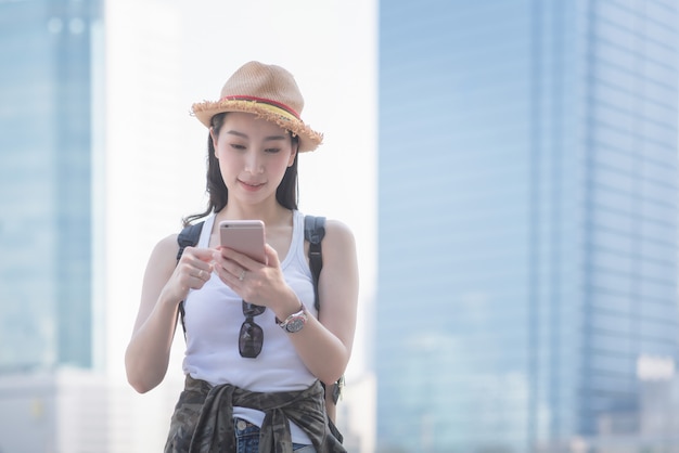 Mujer turística solitaria asiática hermosa que sonríe y que mira el teléfono móvil