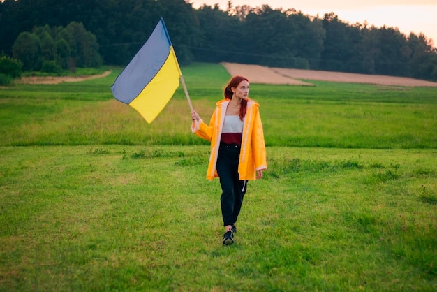 Mujer ucraniana en el campo con una gran bandera de Ucrania Fotos patrióticas Hermosa mujer en un impermeable amarillo