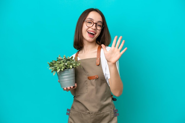 Mujer ucraniana jardinera sosteniendo una planta aislada de fondo azul contando cinco con los dedos