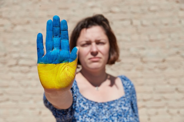 La mujer ucraniana con un símbolo de bandera en la mano muestra una señal de alto contra el cielo azul para detener la guerra