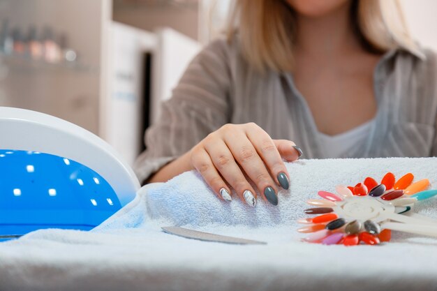 Mujer con uñas acrílicas artificiales adquiere un nuevo color de esmalte durante el procedimiento de manicura. Proceso de manicura en salón de belleza. Belleza de higiene de manos en salón de uñas.