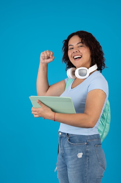 Foto mujer universitaria emocionada y feliz usando una tableta digital y un auricular blanco