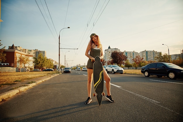 Mujer urbana con un longboard en la carretera en la ciudad