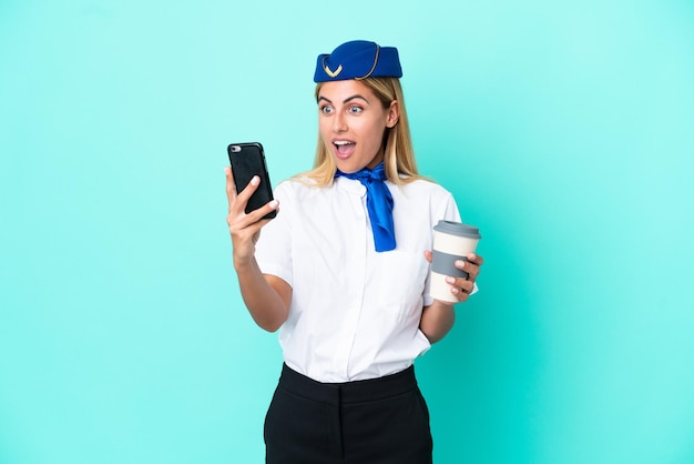 Mujer uruguaya azafata de avión aislada sobre fondo azul sosteniendo un café para llevar y un móvil