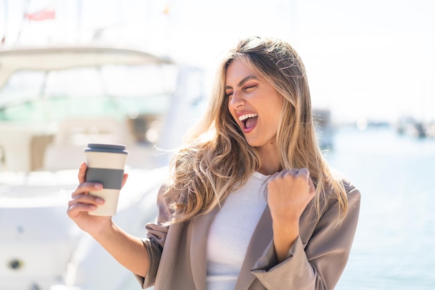 Mujer uruguaya bastante rubia sosteniendo un café para llevar al aire libre celebrando una victoria