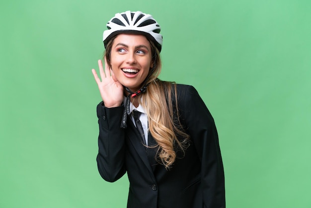 Mujer uruguaya de negocios que lleva un casco de motociclista sobre un fondo aislado escuchando algo poniendo la mano en la oreja