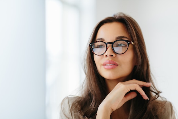 Foto la mujer usa lentes ópticos con marcos oscuros, toca suavemente la barbilla,