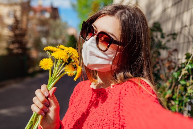 La mujer usa una máscara protectora al aire libre durante el coronavirus covid-19 olores pandémicos flores.