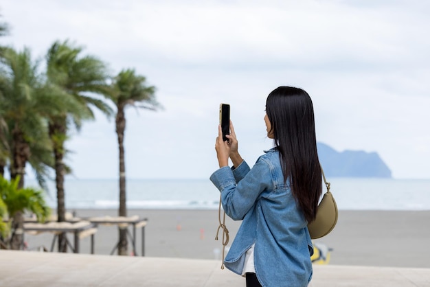 Mujer usa su teléfono móvil para tomar una foto en la playa de arena de Yilan en Taiwán