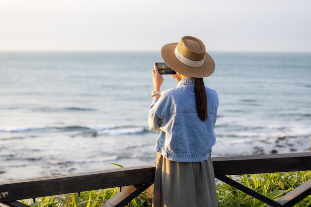 Mujer usa teléfono celular para tomar fotos en la playa del mar