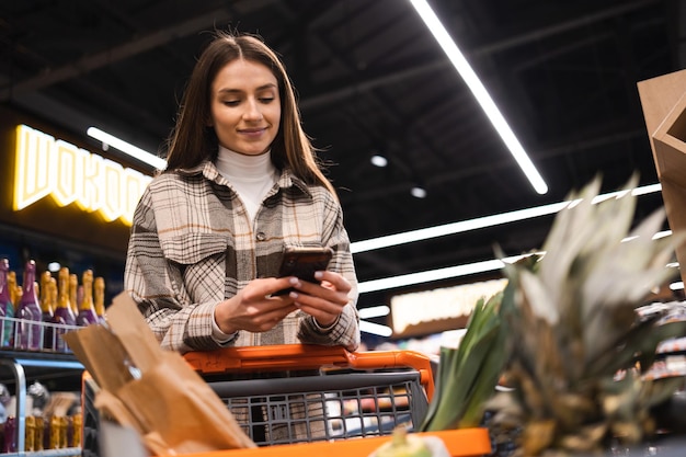 La mujer usa un teléfono inteligente mientras compra en el supermercado