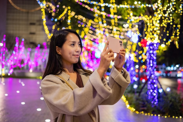 Mujer usa teléfono inteligente para tomar fotos con decoración de luces navideñas