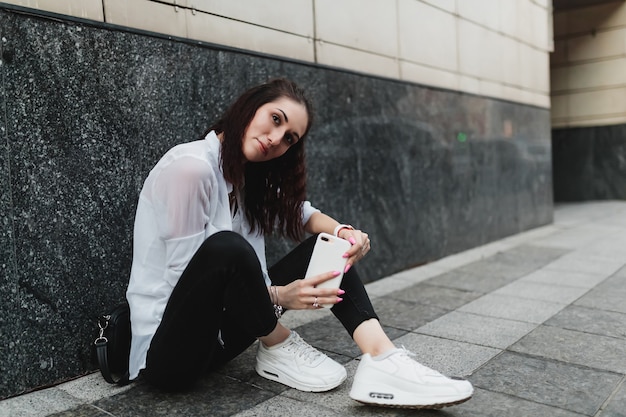 La mujer usa el teléfono mientras está sentada en el suelo. Foto de alta calidad