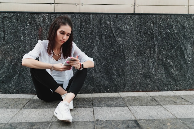 La mujer usa el teléfono mientras está sentada en el suelo. Foto de alta calidad