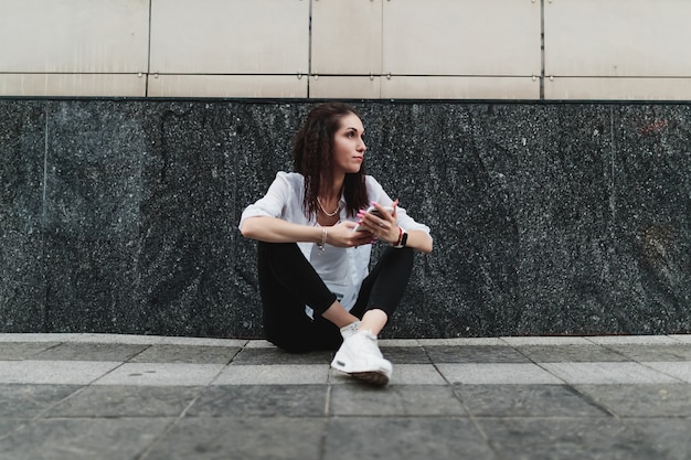 La mujer usa el teléfono mientras está sentada en el suelo. Foto de alta calidad