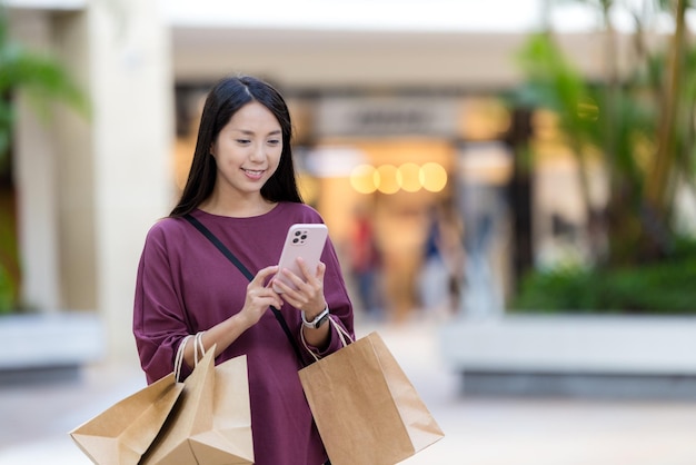 Mujer usa teléfono móvil con bolsa de compras en la plaza