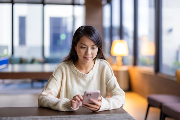 La mujer usa el teléfono móvil y se sienta en la cafetería.