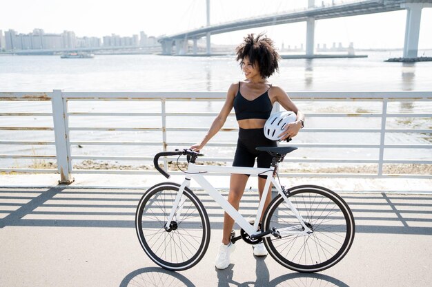 Una mujer usa un transporte ecológico en bicicleta en el entrenamiento cardiovascular de fitness de la ciudad sostiene un casco