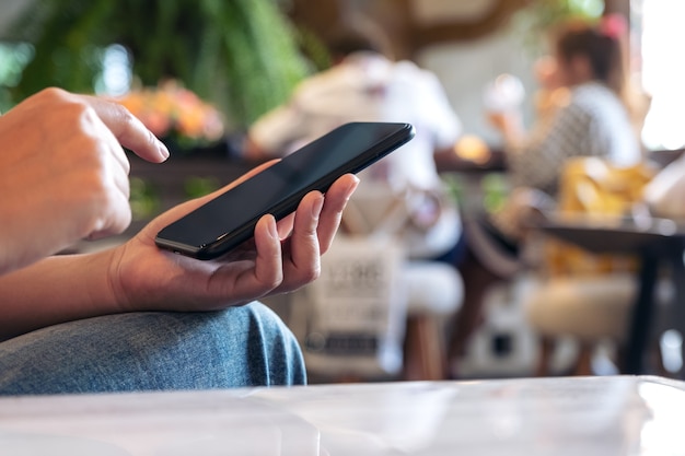 Una mujer usando y apuntando a un teléfono inteligente negro con fondo borroso en el café