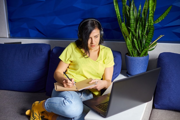 Mujer usando audífonos estudiando en línea usando notebook, laptop, escribiendo notas