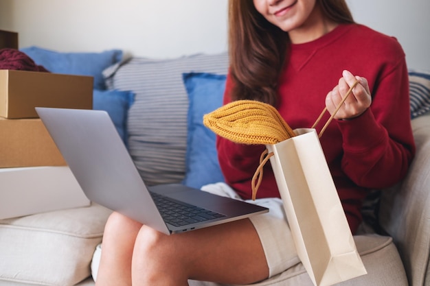 Una mujer usando una computadora portátil para comprar en línea abriendo bolsas de compras y cajas de paquetes postales en casa