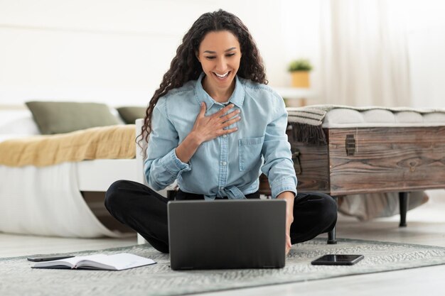 Mujer usando una computadora portátil haciendo videollamadas sentada en el piso