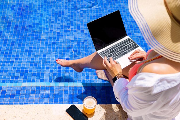 Mujer usando computadora portátil junto a la piscina